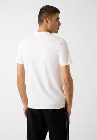 Weißes T-Shirt aus Baumwolle mit kurzen Ärmeln, Rundhalsausschnitt und schmaler Passform. Die Rückseite zeigt eine glatte Oberfläche ohne sichtbare Muster.