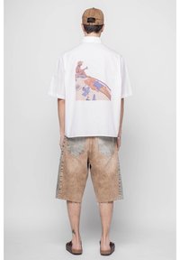 Camicetta bianca a maniche corte con una grafica colorata sul retro, abbinata a pantaloni shorts in denim marroni con un design sbiadito e orli sfrangiati.