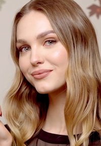 Zbliżenie na osobę z długimi, falującymi, jasnobrązowymi włosami, w przezroczystej czarnej bluzce, o gładkiej cerze i neutralnym kolorze ust.