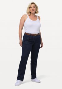 Mörkblå denimjeans med rak benpassform, framfickor och ett brunt bälte, kombinerat med en vit linne och vita sneakers.