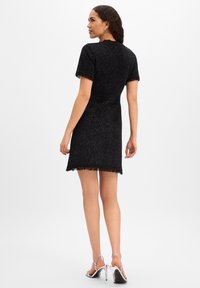 Abito nero corto con maniche corte e bordi con frange, realizzato in un tessuto strutturato che scintilla. Presenta una silhouette aderente e una lunghezza sopra il ginocchio.