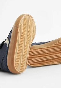 Granatowe zamszowe sneakersy z beżową gumową podeszwą, z wzorem w jodełkę i trójkątnymi akcentami po bokach.