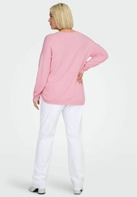 Hellrosa Pullover mit lockerem Schnitt, langen Ärmeln und gerippten Bündchen, kombiniert mit weißer Hose. Der Pullover besticht durch ein schlichtes, sauberes Design.