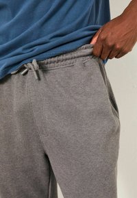 Graue Jogginghose aus geripptem Stoff, mit elastischem Bund, Kordelzug und Seitentaschen, kombiniert mit einem blauen T-Shirt.