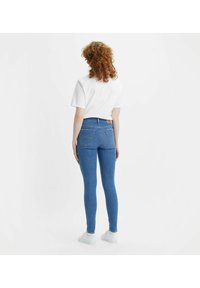 High-waisted blue stretch jeans with a five-pocket design, visible stitching, and a tan brand patch on the back waistband.