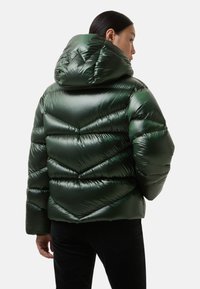 Grøn pufferjakke med hætte, fremstillet af skinnende materiale, med chevron-quiltet mønster og en cropped design. Diskret teksturdetalje.