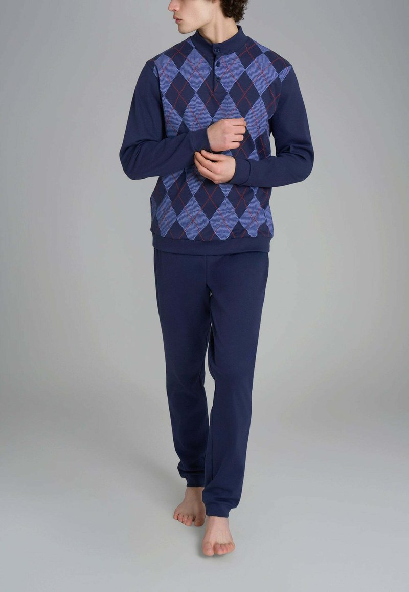 Completo loungewear blu navy composto da un pullover con un motivo di rombi blu, rossi e bianchi, abbinato a pantaloni blu navy uni. Vestibilità morbida e casual.