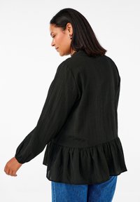 Must mustri tumes blouse, millel on pikad varrukad ja volang/peplum hem; kantud siniste teksadega. Kangas näeb välja kerge ja voolav.