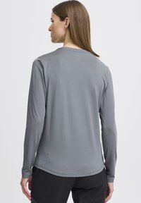 Grijze longsleeve shirt met een gladde textuur en een ronde halslijn, heeft een rechte zoom en contrasterende stiksels bij de naden.