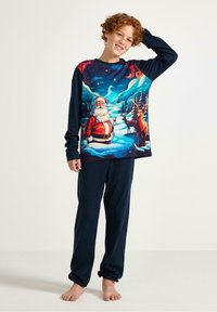Ensemble de pyjama à manches longues avec un graphique de Santa Claus sur le haut, pantalon bleu marine et texture lisse. Les couleurs incluent le rouge, le blanc et le bleu.