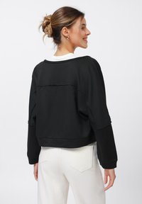 Svart kort sweatshirt med ribbat tyg och vit krage. Stylad med ljusa jeans som har detaljerade bakfickor.