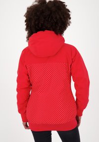 Rode jas met een capuchon, een gestructureerd bovenstuk en een stippenpatroon op de onderste helft. Ribgebreide manchetten en zoom voor een goede pasvorm.