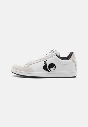 Sneaker in pelle bianca con accenti neri e un distintivo logo di un gallo nero. Punta in suede. Suola piatta bianca. Design con lacci.