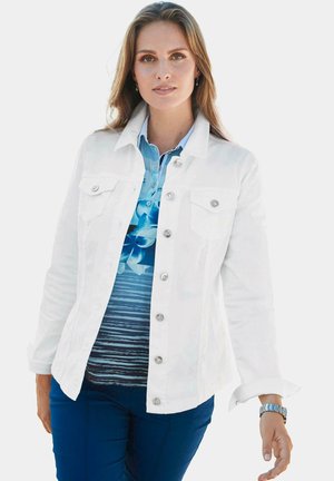 Witte denimjas met zilveren knopen, twee borstzakken, gelaagd over een blauw patronenoverhemd met bloemen en strepen. Marineblauwe broek zichtbaar.