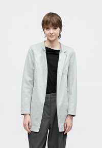 Szürke, hosszú ujjú blézer puha anyagból, laza szabással, felhajtott gallérral és két elülső zsebbel, fekete felsővel és szürke nadrággal párosítva.
