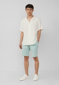 Witte korte- mouw button-up shirt met textuurstof, gecombineerd met lichte muntgroene shorts en witte sneakers, wat een casual ensemble creëert.