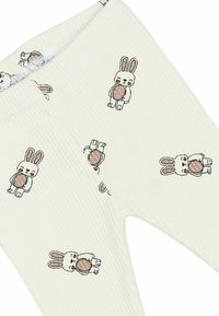 White ribbed leggings with a repeating pattern of cartoon rabbits holding brown eggs. Elastic waistband, soft texture, suitable for casual wear.
