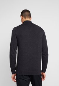 Mørkegrå pullover med lange ærmer og en flad krave, der har en tekstureret strik og ribbede manchetter. Enkel og minimalistisk design.