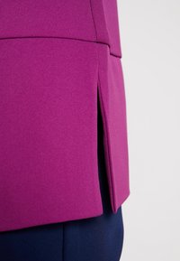 Fioletowy materiał o strukturalnym wzorze z bocznym rozcięciem. Tkanina ma gładką teksturę, uzupełnioną kontrastującym, ciemnoniebieskim tłem.