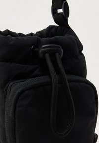 Czarna materiałowa torba z przednią kieszenią na zamek oraz regulowanym ściągaczem ze stopką na białym tle.