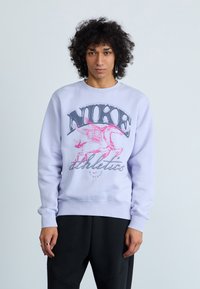 Világoslila pulóver, grafikus nyomattal, amelyen egy rózsaszín szárnyas ló és a "NIKE athletics" felirat található, puha anyagból készült, kerek nyakú kialakítással.