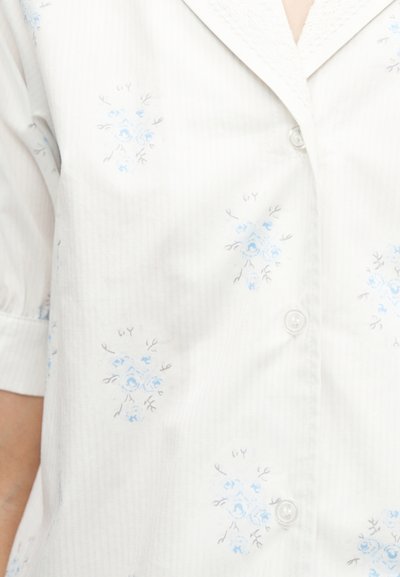 Λευκό πουκάμισο με κοντά μανίκια, με μικρά μπλε λουλουδάτα σχέδια και γιακά με δαντέλα.