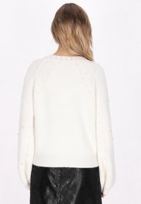 Pulover crem dintr-un material tricotat texturat, cu un croi supradimensionat, decorat cu mici accente asemănătoare perlitelor pe mâneci și cu tiv ondulat.