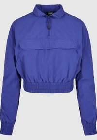 Kuttet lilla jakke laget av lett stoff, med halv-zip krage, elastisk midje og en frontlomme.
