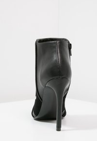 Bota negra de tobillo con tacón alto de estilo stiletto, confeccionada en cuero liso y paneles de tela texturizada, con cremallera lateral y diseño de punta redondeada.