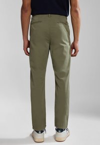 Pantalones de chándal de color verde oliva, de corte relajado, con frente plano, dos bolsillos traseros y costuras visibles. Llevados con zapatillas blancas y marinas.