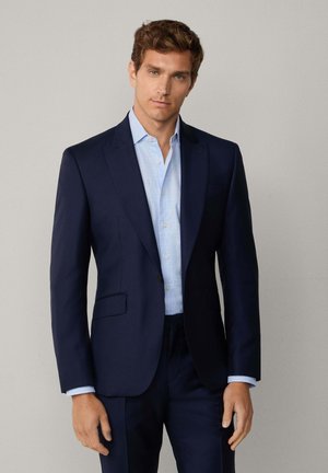 Marineblauer Anzugjackett mit aufgesetztem Revers, einer Knopfleiste und zwei Fronttaschen. Darüber ein hellblaues kariertes Hemd getragen. Glatter Stofftextur.