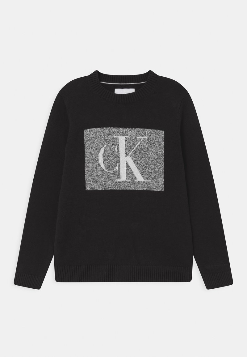 Černý svetr s kulatým výstřihem, na přední straně je šedý pletený obdélník s bílými písmeny "CK". Žebrované manžety a lem.
