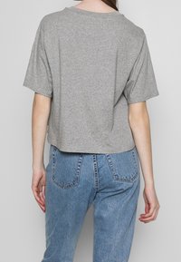 Camiseta gris corta hecha de tejido suave, con mangas cortas, un cuello redondeado y un corte holgado. Se lleva con vaqueros de tiro alto azul claro.