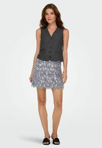 Pelēks bezroku vestes ar pogām komplekts ar teksturētu pelēku spalvām rotātu svārku ar spīdumiem un melnām slidināmajām sandales.