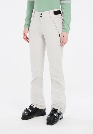 Helle beigen Skihosen mit slim fit, ausgestattet mit Reißverschlusstaschen, einer glatten Textur und einem verstellbaren Bund, kombiniert mit schwarzen Skischuhen.