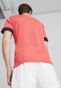 Czerwony dresowy podkoszulek o siateczkowej strukturze i czarnych akcentach na rękawach. Z tyłu znajduje się minimalne logo, zaprojektowany z myślą o komforcie i wentylacji.