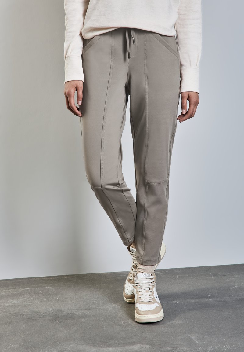 Ljust grå joggerbyxor med snäva ben, subtil sömdekoration och resårmidja. Bärs med beige hög-top sneakers.