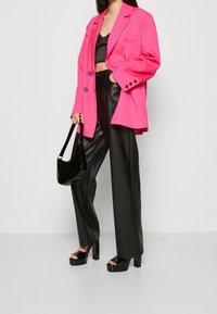 Rosa överdimensionerad kavaj, svart cropped topp, svarta vida byxor i fuskskinn och svarta lackade plattformssandaler. Svart axelväska.