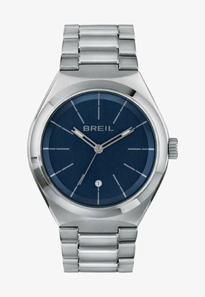 Kello on hopeanvärinen ruostumattomasta teräksestä, jossa on pyöreä sininen teksturoitu kellotaulu, valkoiset tuntimerkit ja päivämääränäyttö kuuden kohdalla. Varustettu metalliketjuhihnalla.