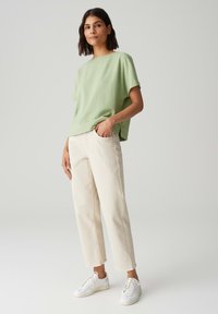 Haut texturé vert clair à manches courtes, pantalon crème à jambes droites et baskets blanches. Le haut présente une coupe décontractée avec des fentes sur les côtés.