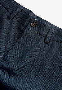 Pantaloni blu navy con motivo testurizzato, dotati di chiusura con bottone marrone e passanti per cintura. Il tessuto appare liscio e resistente.
