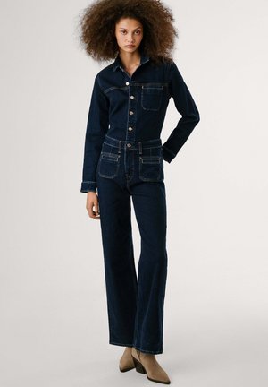 Salopette en denim bleu foncé avec manches longues, col, boutons sur le devant et deux poches poitrine. Design à jambes droites avec des détails de couture subtils.