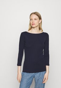 Top justo de manga longa azul-marinho com decote barco e textura suave, combinado com calças texturizadas azul-claro.