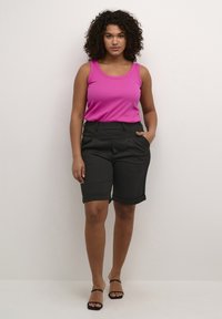 Débardeur sans manches rose avec un col rond, associé à un short noir taille genoux ajusté avec des poches latérales et des ourlets retroussés.