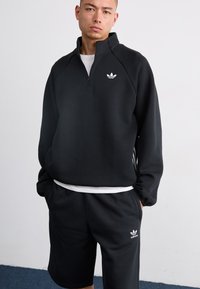 Black athletic sweatshirt with a quarter-zip collar and white logo; paired with matching black shorts. Soft fabric with a relaxed fit.