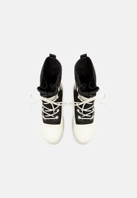 Paire de baskets montantes noires et blanches avec des lacets blancs, vue de dessus sur un fond clair uni.