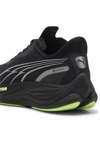 Crna atletska cipela s mrežastim gornjim dijelom, srebrnim detaljima, teksturiranom potplatom i zelenim detaljima na donjem dijelu; ima Gore-Tex oznaku.