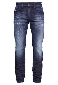 Mörkblå denimjeans med slitna detaljer, en tapered passform och ljus blekning. Har fem fickor och framknäppning.