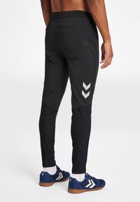 Schwarze Sporthosen mit schmalem Schnitt, ausgestattet mit einem strukturierten Design, elastischem Bund und reflektierenden Chevron-Akzenten an den Seiten.