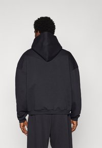 Sudadera con capucha gris oscuro de corte relajado, con puños y dobladillo acanalados, textura suave y diseño minimalista.